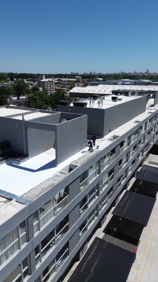 Vista aérea de operarios aplicando membrana líquida blanca con rodillo en la terraza de un edificio en Neuquén