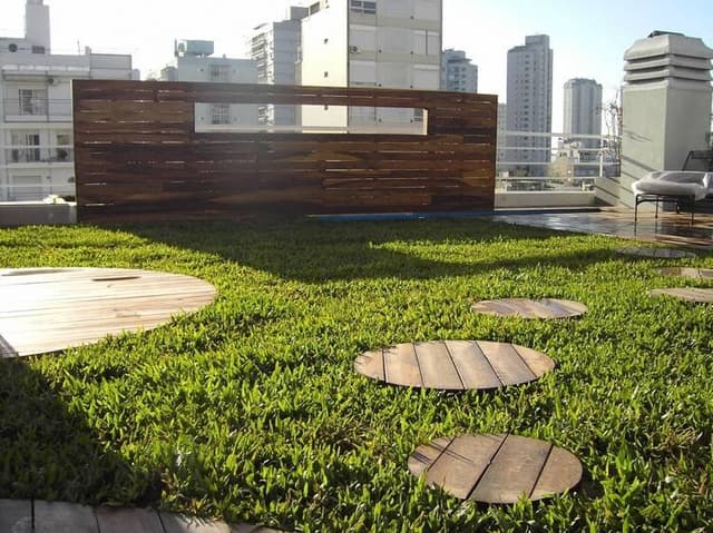 Terraza ajardinada con césped y canteros en edificio urbano